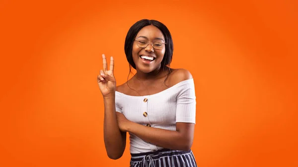 Positivo nero ragazza gesturing v-sign standing su arancio studio sfondo — Foto Stock