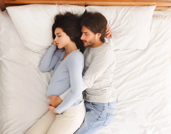 Αγαπημένος σύζυγος αγκαλιάζει την έγκυο γυναίκα του ενώ κοιμούνται στο κρεβάτι — Φωτογραφία Αρχείου