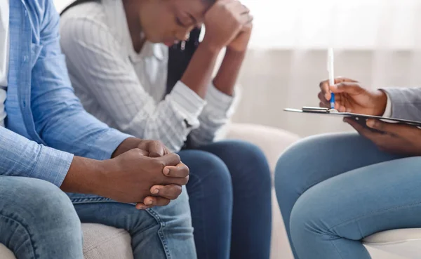 Unrecognizable psychologist noting down problems of young african american spouses