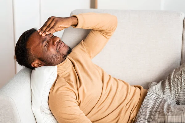Парень с головной болью касается лба, лежащего на диване дома — стоковое фото