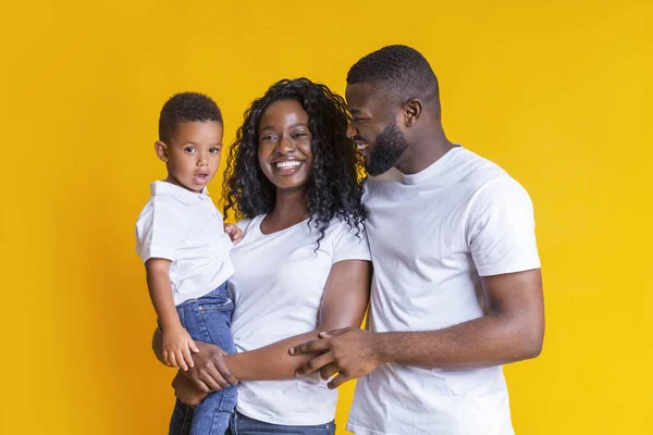 Feliz familia negra con su pequeño hijo sonriendo y abrazándose sobre fondo amarillo — Foto de Stock