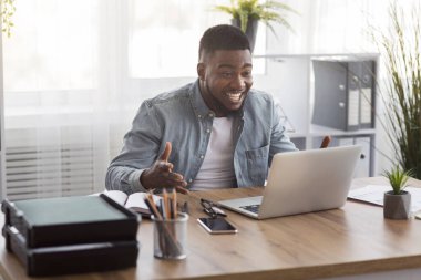 Mutlu afro iş adamı iyi haberlerden heyecanla dizüstü bilgisayarına bakıyor.