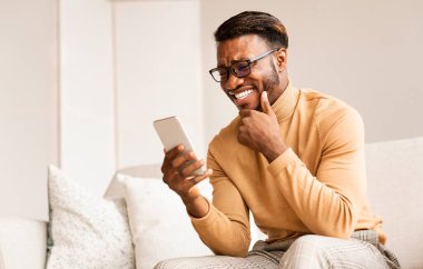 Afro adam cep telefonu kullanıyor. Evde oturmuş komik haberler okuyor.