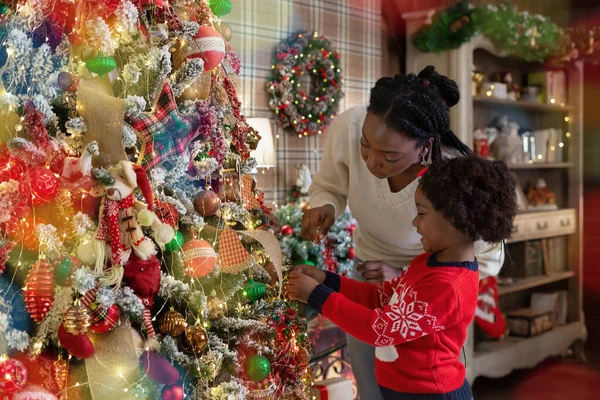 Pequena menina afro decoração árvore de Natal com a mãe em casa — Fotografia de Stock