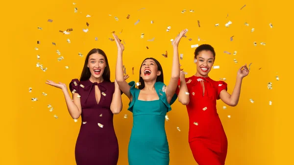Drei multiethnische Mädchen in Kleidern, die Spaß unter fallendem Konfetti haben, Studio — Stockfoto