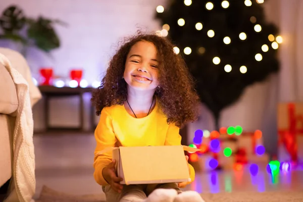 Criança africana feliz abrindo presente de Natal perto da árvore decorada — Fotografia de Stock