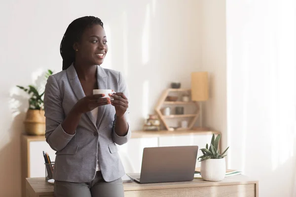 Black female employee drinking coffee in office, having break in work