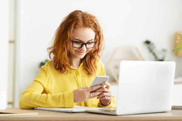 Empresária feliz usando smartphone perto do computador no escritório — Fotografia de Stock