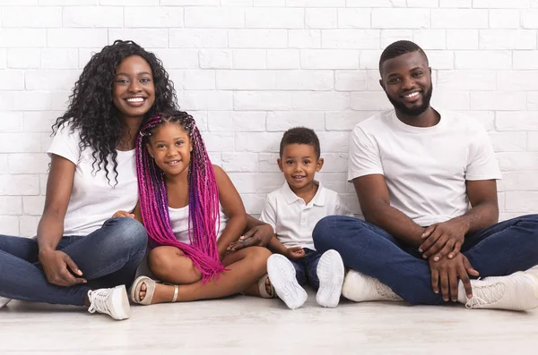Usmívající se černí rodiče se dvěma malými dětmi sedícími spolu na podlaze — Stock fotografie