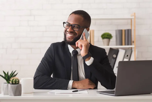 Glücklicher schwarzer Unternehmer, der angenehme Gespräche mit Kollegen am Telefon führt — Stockfoto