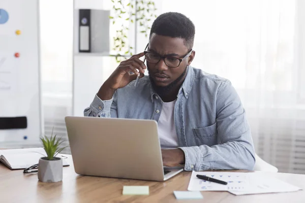 Berörd svart anställd talar på mobiltelefon och tittar på bärbar skärm — Stockfoto