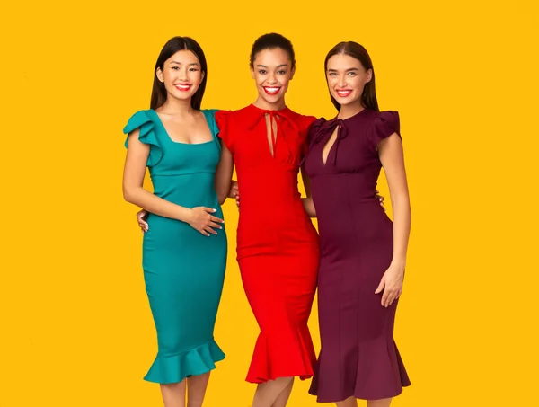 Три разные девушки в гламурных платьях позируют на жёлтом фоне — стоковое фото