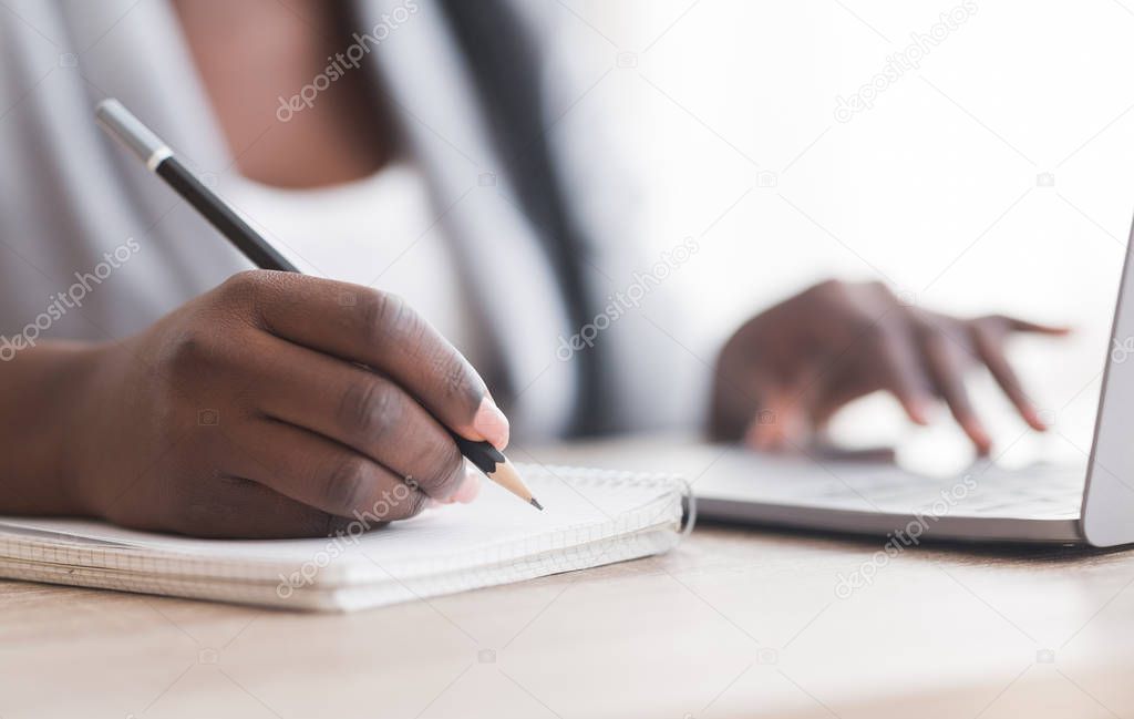 Unrecognizable female employee taking notes while working on laptop in office