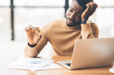 Üzgün Afrikalı Amerikalı adam elinde altın Bitcoin tutuyor.