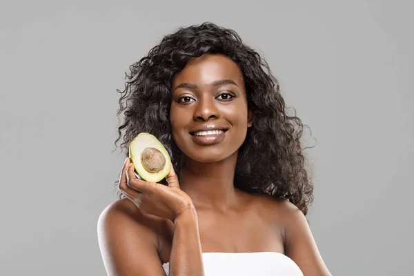 Portret van aantrekkelijke zwarte vrouw met avocado helft over grijze achtergrond — Stockfoto