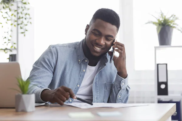 Empresario africano hablando con compañero por teléfono y revisando informes financieros —  Fotos de Stock