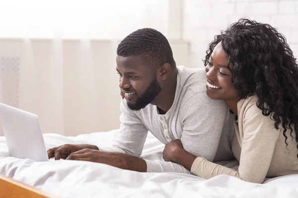 Vrolijke afro echtgenoten liggen in bed met behulp van laptop samen — Stockfoto