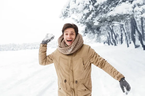 Feliz joven lanzando bola de nieve mirando a la cámara en el bosque —  Fotos de Stock