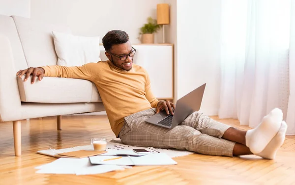 Feliz empresario afro trabajando en el ordenador portátil sentado en el piso interior — Foto de Stock