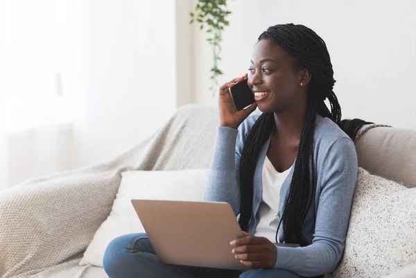 Schwarze Millennial-Frau telefoniert mit Handy und benutzt Laptop zu Hause — Stockfoto