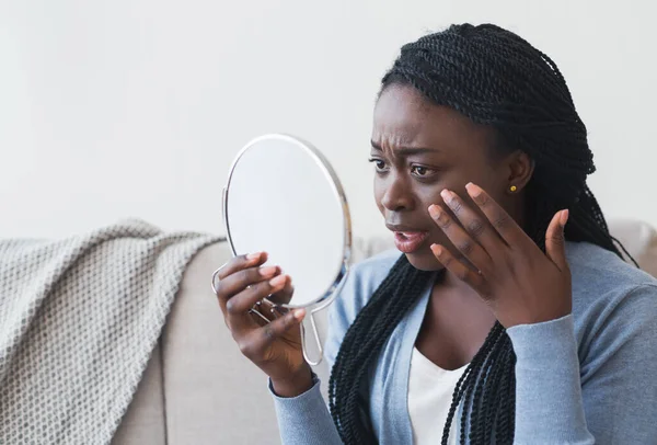 Mujer afro decepcionada mirando al espejo y tocando su piel —  Fotos de Stock