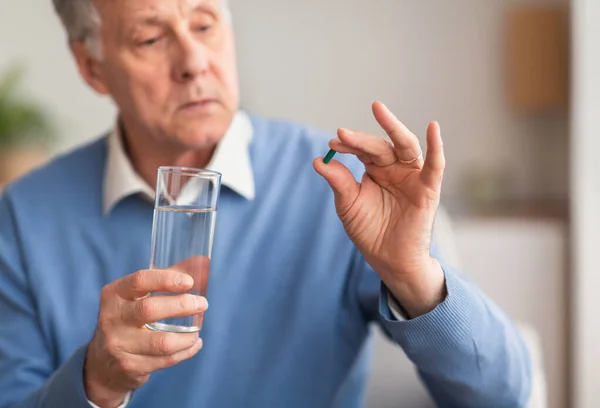 Äldre man håller ett piller och glas vatten inomhus — Stockfoto