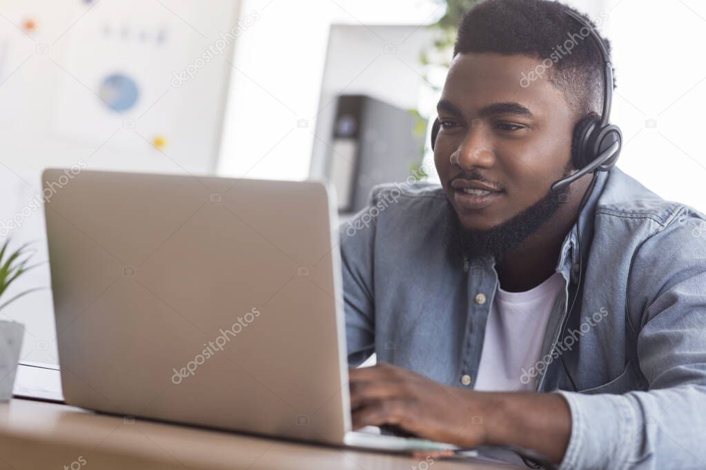 Handsome call center manager wearing headset and typing at laptop