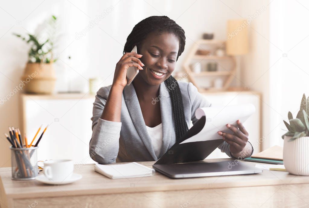 Black female manager making phone call and checking reports in office