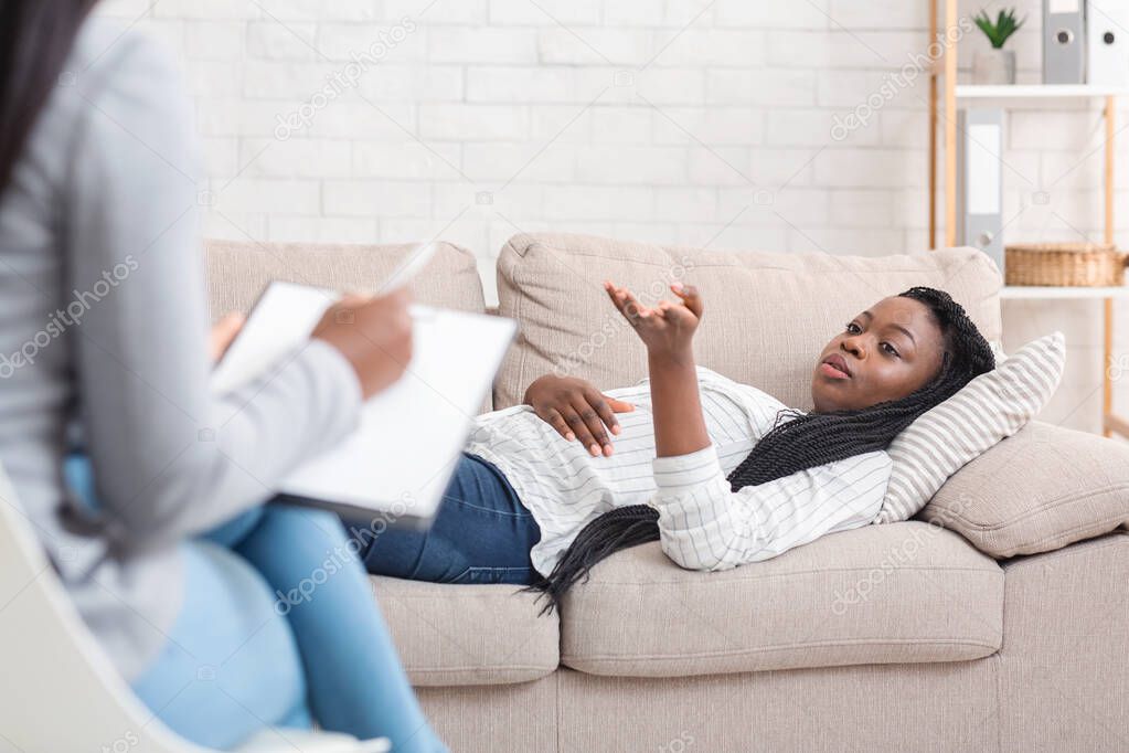 Young black woman lying on couch, sharing problems at counselors office