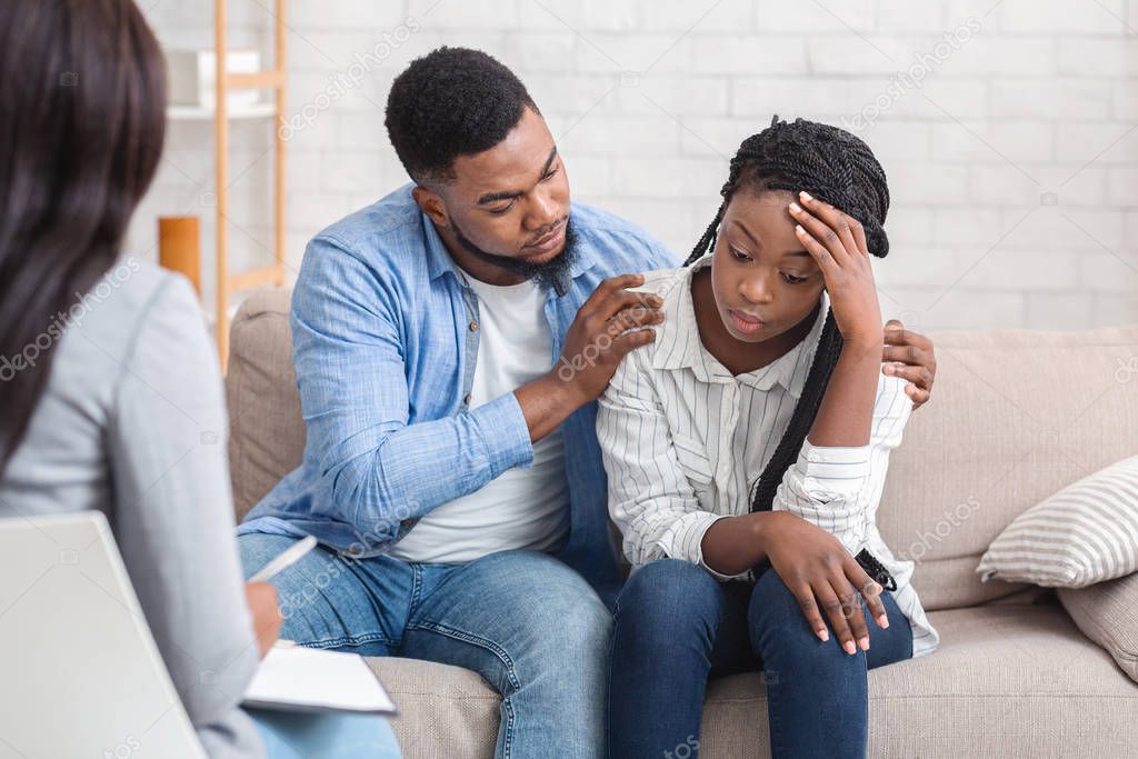 Loving husband supporting his depressed wife during psychotherapy session with counselor
