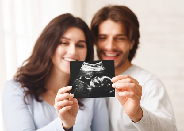 Happy young couple looking at sonography picture of their baby — ストック写真