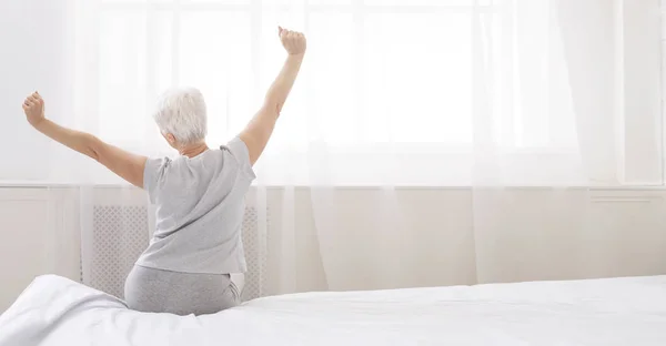 Mujer mayor bien dormida estirándose con los brazos levantados en la cama —  Fotos de Stock