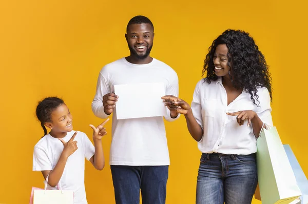 Vreugdevolle familie wijzen naar witte reclamebord en het houden van boodschappentassen — Stockfoto