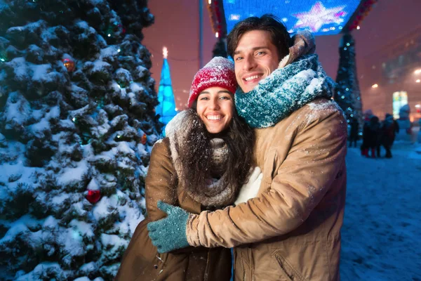 Alegre pareja abrazando sonriente de pie cerca del árbol de Navidad en la ciudad —  Fotos de Stock