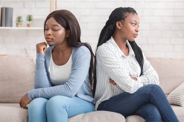 Offended girlfriends sitting back to back, ignoring each other after quarrel clipart
