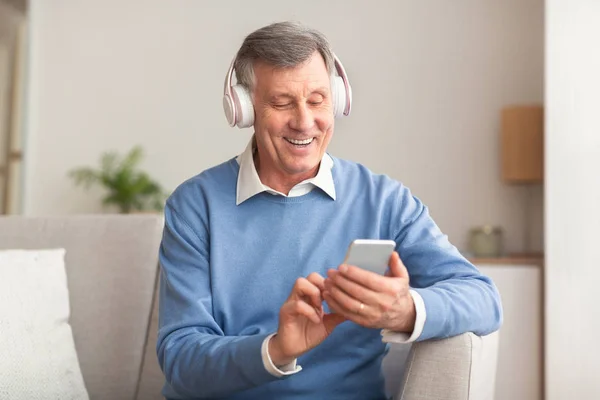 Älterer Mann hört Lied mit Smartphone auf Couch — Stockfoto