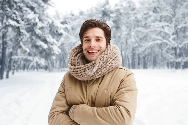 Hombre atractivo sonriendo ante la cámara posando en el bosque nevado —  Fotos de Stock