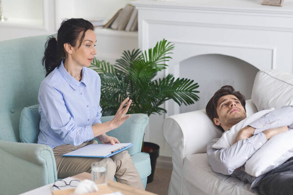 Тяжелый депрессивный мужчина лежит на диване в кабинете терапевта
