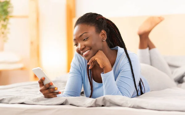 Chica negra usando Smartphone acostado en la cama en casa —  Fotos de Stock