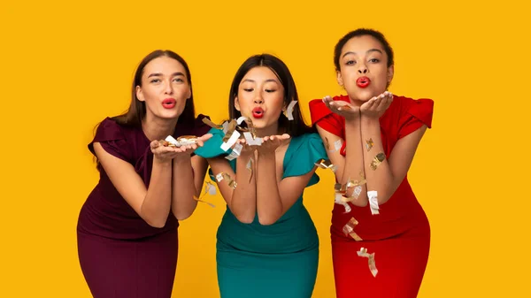 Three Girls In Dresses Blowing Confetti From Hands In Studio — Stock Photo, Image