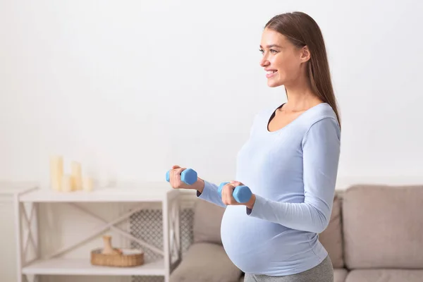 Vista lateral de la niña embarazada levantando pesas azules — Foto de Stock