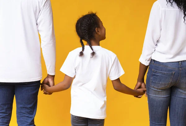 Pequena menina negra de mãos dadas de sua mãe e pai, visão traseira — Fotografia de Stock
