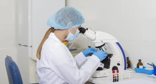 Asistente femenina borrosa en ropa protectora mirando al microscopio —  Fotos de Stock