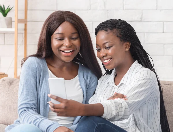 Duas namoradas negras alegres tomando selfie, sentadas no sofá em casa — Fotografia de Stock