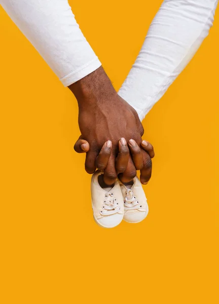 Руки черной пары держат детские сапоги вместе — стоковое фото