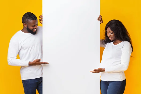 Zwanger paar demonstreren blanco bord over gele achtergrond — Stockfoto