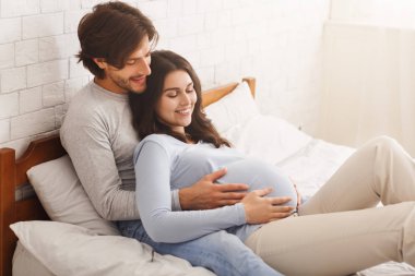 Genç hamile kadın kocasıyla yatakta dinleniyor.