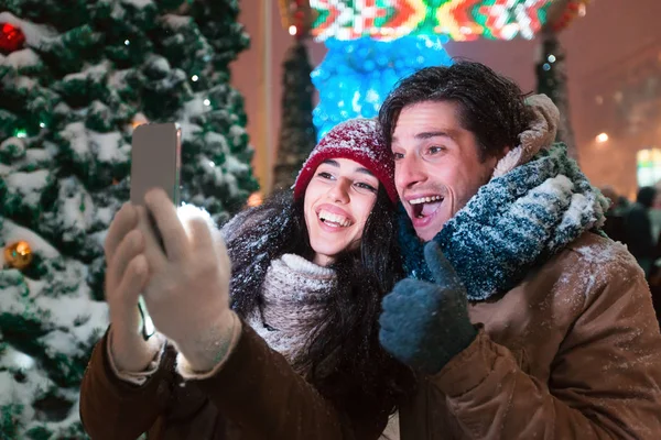 Pareja haciendo selfie de pie junto al árbol de Navidad en la ciudad —  Fotos de Stock