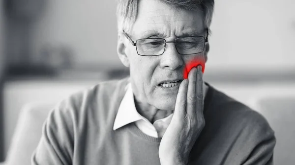 Senior Man lijdt aan tandpijn zittend op de bank binnen, zwart-wit — Stockfoto