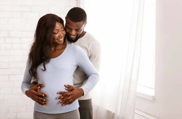 Hamile afro kadın ve kocası evde sarılıyorlar. — Stok fotoğraf